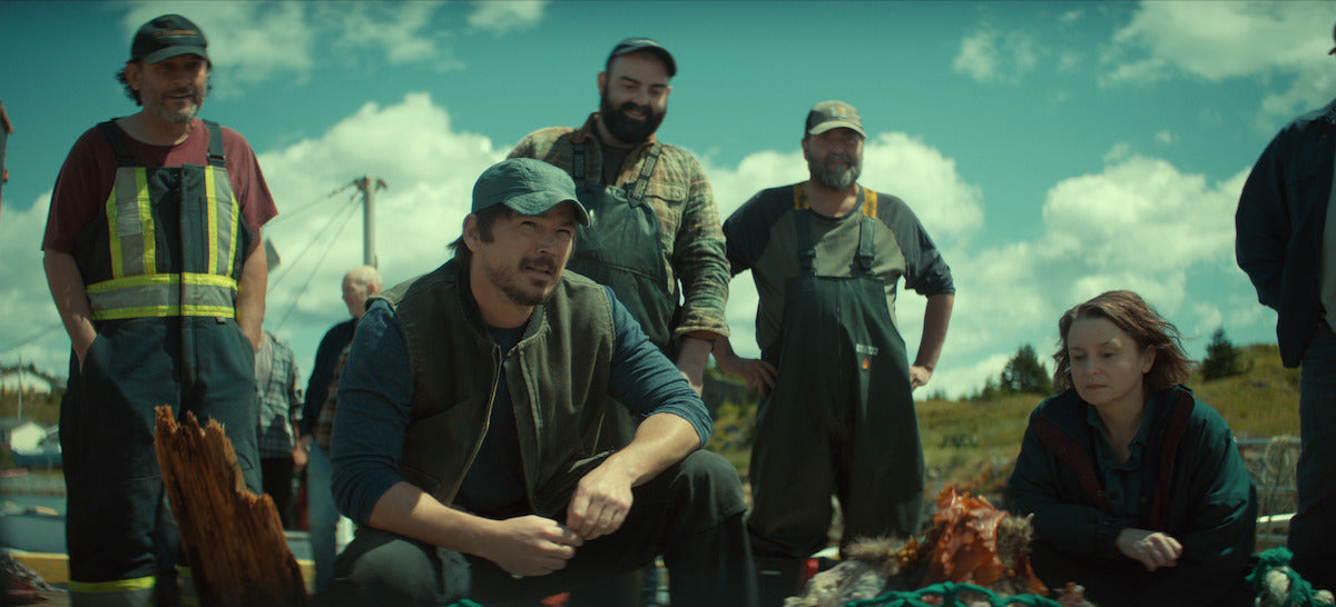 Local fishing workers and a woman from Netflix's Below gathered outdoors by fishing equipment