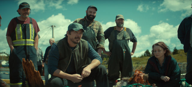 Local fishing workers and a woman from Netflix's Below gathered outdoors by fishing equipment