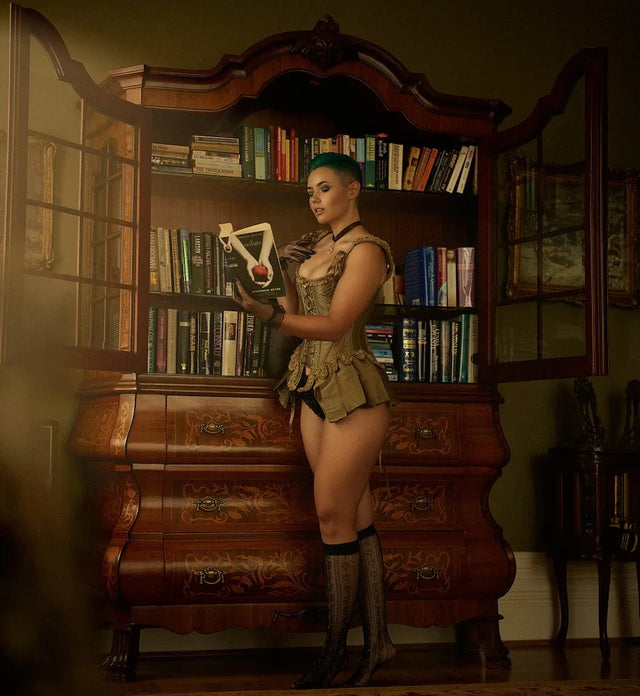 Kit Barrus in a corset-inspired outfit posing in front of a bookcase; image from her official website