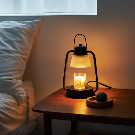 Vintage lantern-style candle warmer lamp glowing on a wooden bedside table