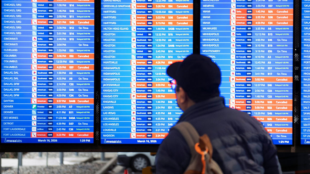 Passengers check a US airport arrivals board showing delayed and canceled flights